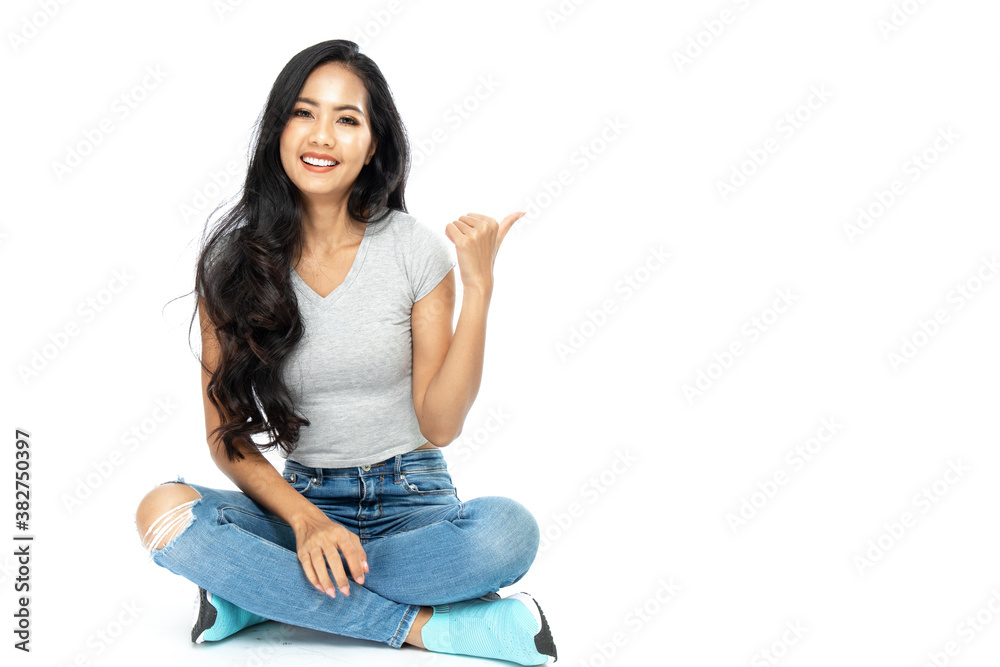 A young Asian woman wore a casual dress sit on the floor. She pointed her finger to the side space. Isolated on white background. Isolated on white background