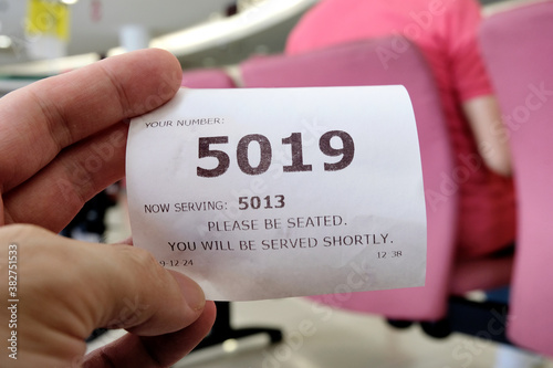 Hand holding a queue number ticket for a counter service at a bank while waiting turn to be attended to. A queue ticket showing the current waiting number been assigned.