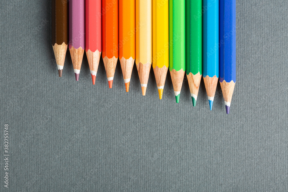 colored pencils lined up in row on gray background colored pencils lined up in row on gray background