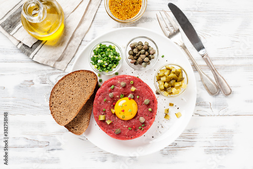 Wallpaper Mural Beef tartare with capers , fresh onion and pickled cucumber on white plate on white wooden background.	 Torontodigital.ca