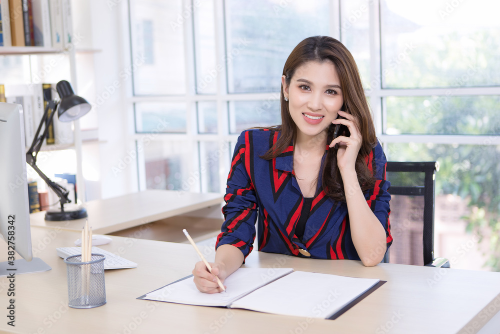 Beautiful Asian businesswoman holds a smartphone to talk about work.Work from home Beautiful Asian businesswoman holds a smartphone to talk about work.Work from home