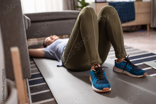 A sporty woman in sportswear is rest on the floor with dumbbells and is using a laptop at home in the living room. Exercise indoors during quarantine. Exercise, Workout at home activities.