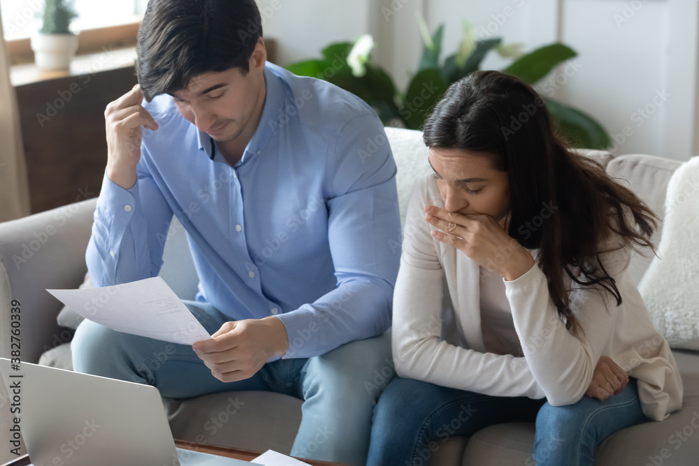 Terms and conditions. Thoughtful pensive young family husband and wife studying careful financial documents of getting mortgage or loan, hesitating while choosing bank deposit, planning monthly budget Terms and conditions. Thoughtful pensive young family husband and wife studying careful financial documents of getting mortgage or loan, hesitating while choosing bank deposit, planning monthly budget