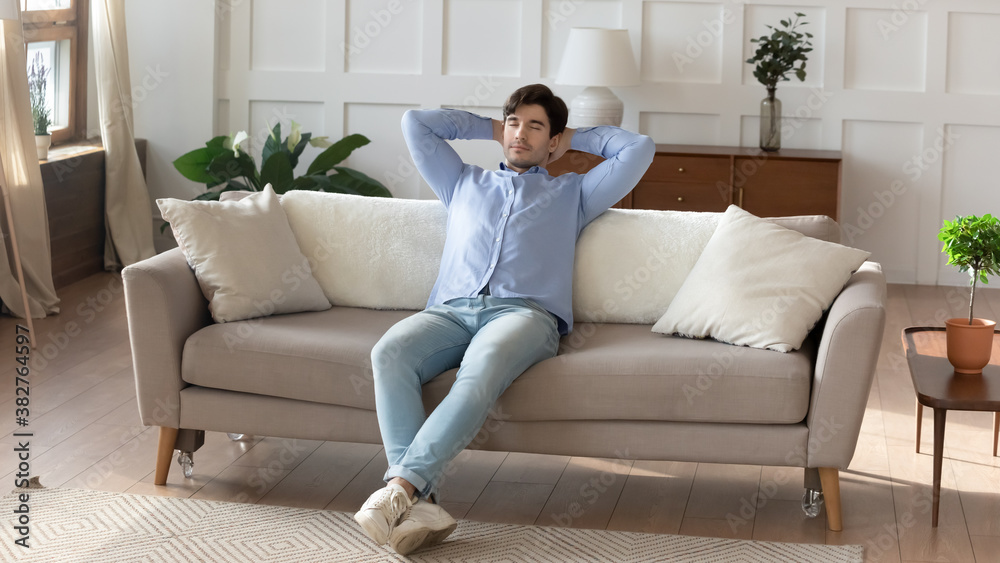 What a good day! Carefree relaxed millennial man resting on sofa at modern living room in comfy pose, taking a break from work on weekend, dreaming and planning for future, breathing cool fresh air What a good day! Carefree relaxed millennial man resting on sofa at modern living room in comfy pose, taking a break from work on weekend, dreaming and planning for future, breathing cool fresh air