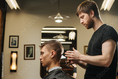 Keen hairdresser making a haircut for a young man in a barber shop