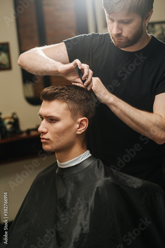 Against the light image of hairdresser combing young man's hair in a barber shop