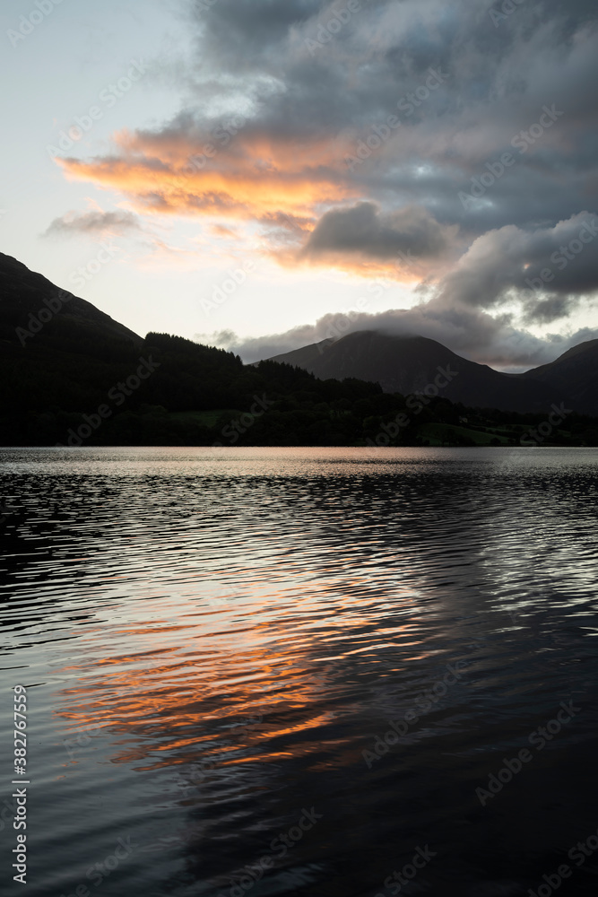 Beautiful sunrise landscape image looking across Loweswater in the Lake District towards Low Fell and Grasmere with vibrant sunrise sky breaking on the mountain peaks