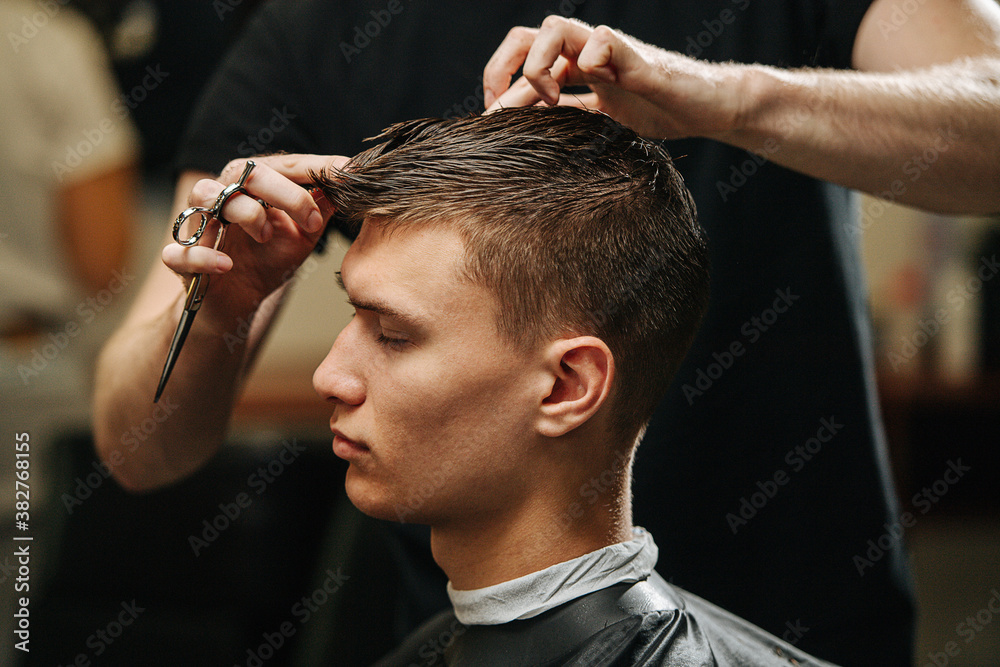 Relaxed young male client getting haircut in a barber shop Relaxed young male client getting haircut in a barber shop