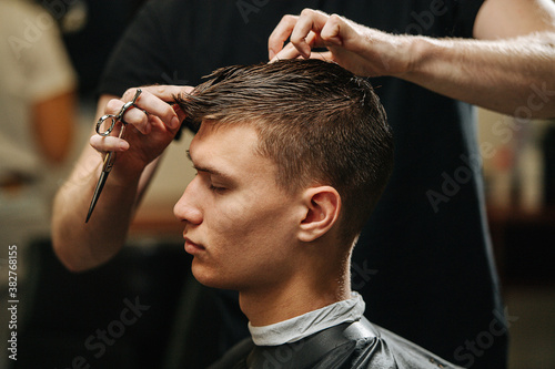 Relaxed young male client getting haircut in a barber shop