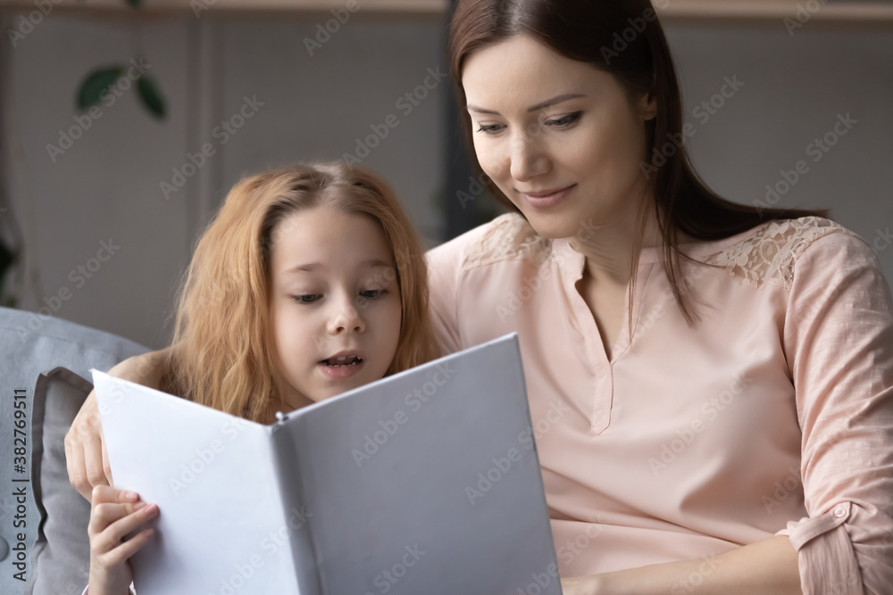 Close up loving mother and pretty little girl child reading book together, sitting on cozy couch in living room, caring mom teaching preschool daughter, family enjoying leisure time at home Close up loving mother and pretty little girl child reading book together, sitting on cozy couch in living room, caring mom teaching preschool daughter, family enjoying leisure time at home