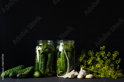 Preparing pickled cucumbers with herbs, garlic and dill. Marinated cucumber gherkins in glass jar on black background. Homemade preserves