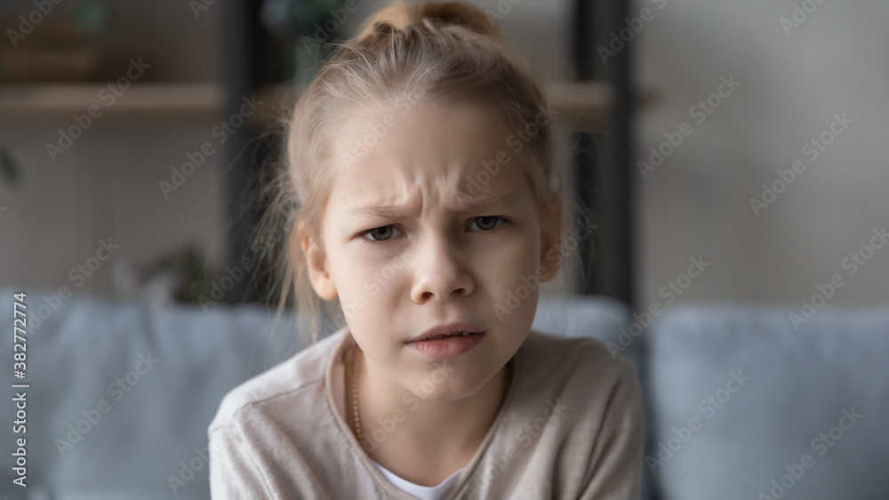 Head shot portrait close up unhappy little girl looking at camera, sitting on couch at home, pretty child making video call, having problem with webcam, shooting recording for social network Head shot portrait close up unhappy little girl looking at camera, sitting on couch at home, pretty child making video call, having problem with webcam, shooting recording for social network