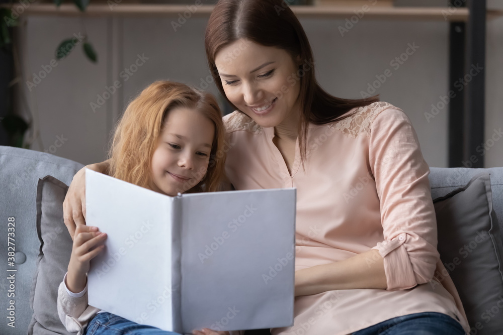 Smiling young mother teaching little daughter to read, sitting on cozy couch at home together, enjoying leisure time, interesting story, pretty preschool girl holding book, children education Smiling young mother teaching little daughter to read, sitting on cozy couch at home together, enjoying leisure time, interesting story, pretty preschool girl holding book, children education