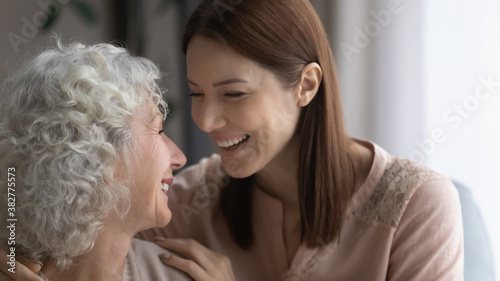 Close up overjoyed young woman with mature mother laughing, having fun, enjoying leisure time together, excited happy elderly female with adult daughter or granddaughter chatting, hugging