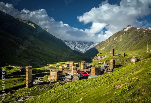 Panoramic view on small Ushguli village located in the downhill and surrounded with green hills in the sunrise against blue sky in Georgia. photo