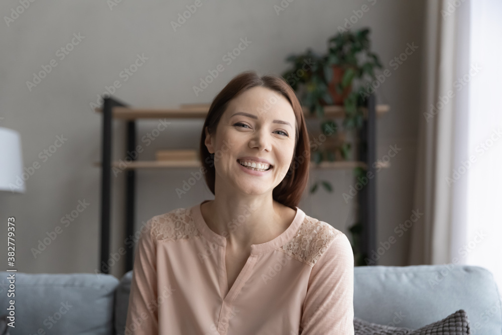 Head shot portrait smiling young woman sitting on couch at home, looking at camera, happy beautiful girl shooting video for social network, chatting online, teacher coach recording tutorial Head shot portrait smiling young woman sitting on couch at home, looking at camera, happy beautiful girl shooting video for social network, chatting online, teacher coach recording tutorial