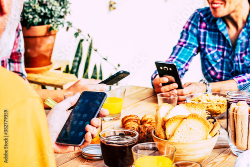 Close up of group of people use phone at the table while have breakfast together - addicted generation to internet web device - share and live on social media concept photo