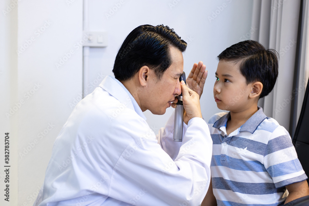 An Asian male doctor uses An ophthalmoscope to examine the boy's eyes. The ophthalmologist examines the child's vision. An Asian male doctor uses An ophthalmoscope to examine the boy's eyes. The ophthalmologist examines the child's vision.