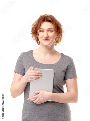 Red haired adult mature woman in gray dress with mobile tablet in her hands smiling