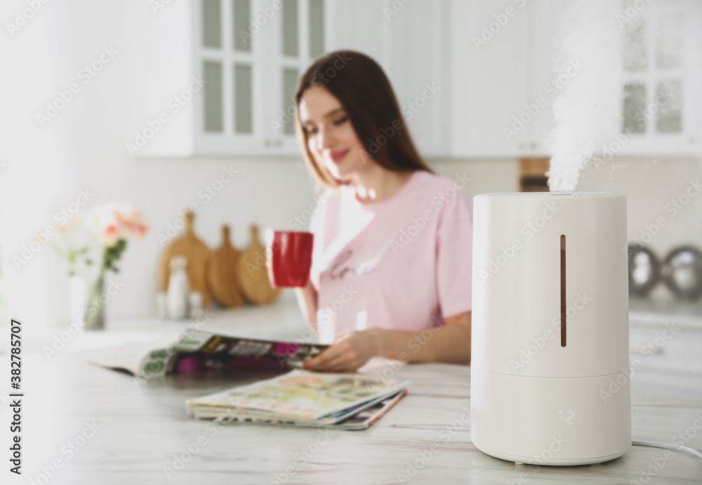 Modern air humidifier and blurred woman drinking coffee in kitchen