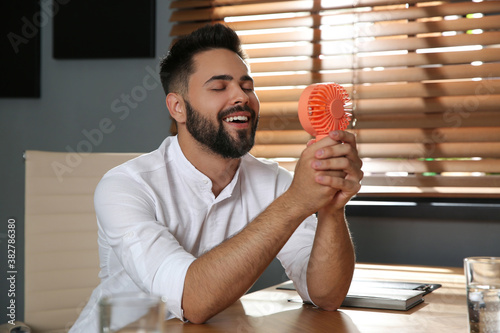 Man enjoying air flow from portable fan at workplace. Summer heat