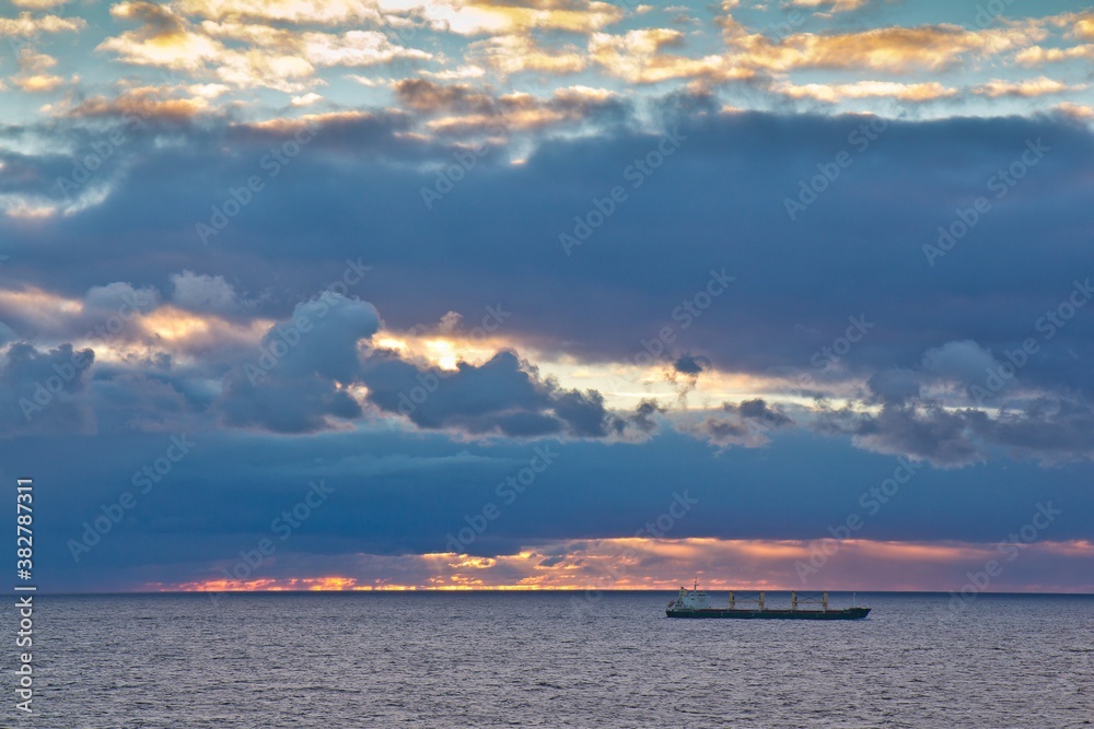 A cargo ship floating afar in the Baltic sea against cloudy sky at sunset. A cargo ship floating afar in the Baltic sea against cloudy sky at sunset.
