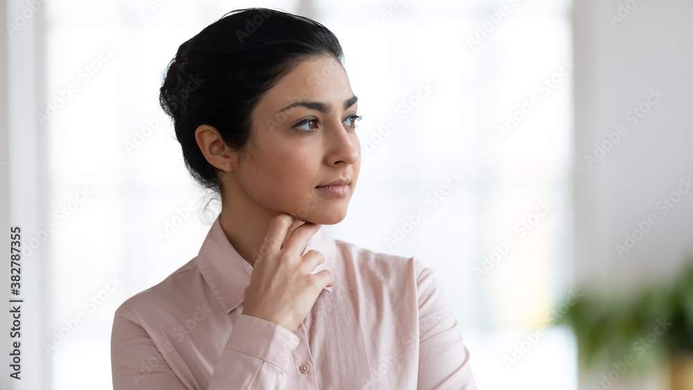 Close up of pensive young indian woman look in distance thinking or dreaming indoors. Thoughtful millennial mixed race ethnicity female lost in thoughts, pondering planning. Business vision concept. Close up of pensive young indian woman look in distance thinking or dreaming indoors. Thoughtful millennial mixed race ethnicity female lost in thoughts, pondering planning. Business vision concept.