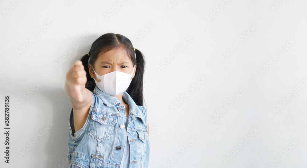 Asian child unlike thumb down or kid girl unhappy angry wearing N95 white face mask for close mouth nose with flu cough sick and protect PM 2.5 dust or coronavirus covid-19 on wall space background