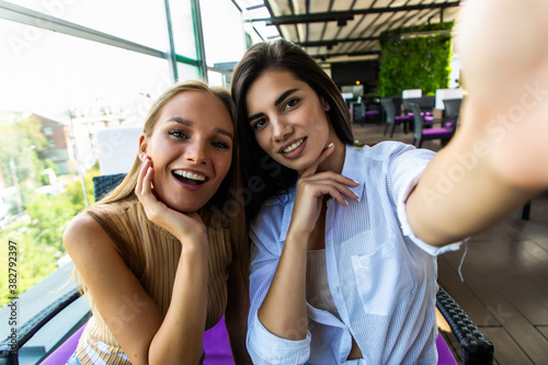 Two smiling women friends driniking coffee and taking selfie, friendship concept