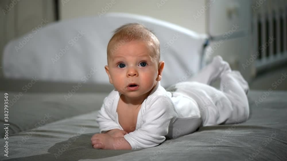 The child lies on his stomach on the sofa in the bedroom and looks at the camera