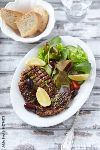 Grilled pork steak with fresh salad. Bright wooden background. Top view.