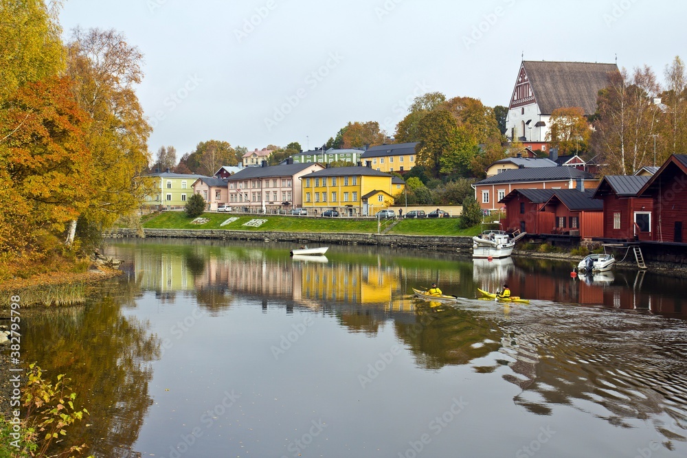 Obraz premium PORVOO, FINLAND - OCTOBER 15, 2015. Two men in canoe sailing in the river reflecting houses on the embankment and yellow trees in autumn in Porvoo, Finland.