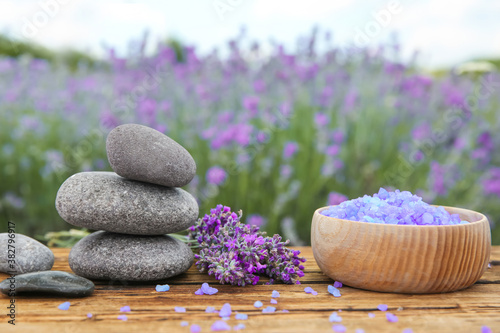 Spa stones  fresh lavender flowers and bath salt on wooden table outdoors  closeup