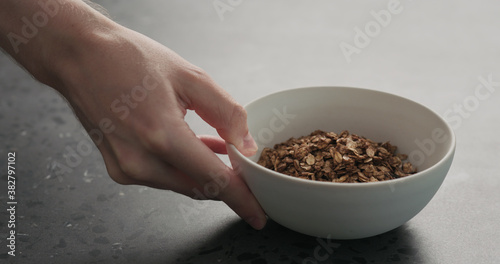 man hand place white bowl with chocolate granola on a concrete countertop