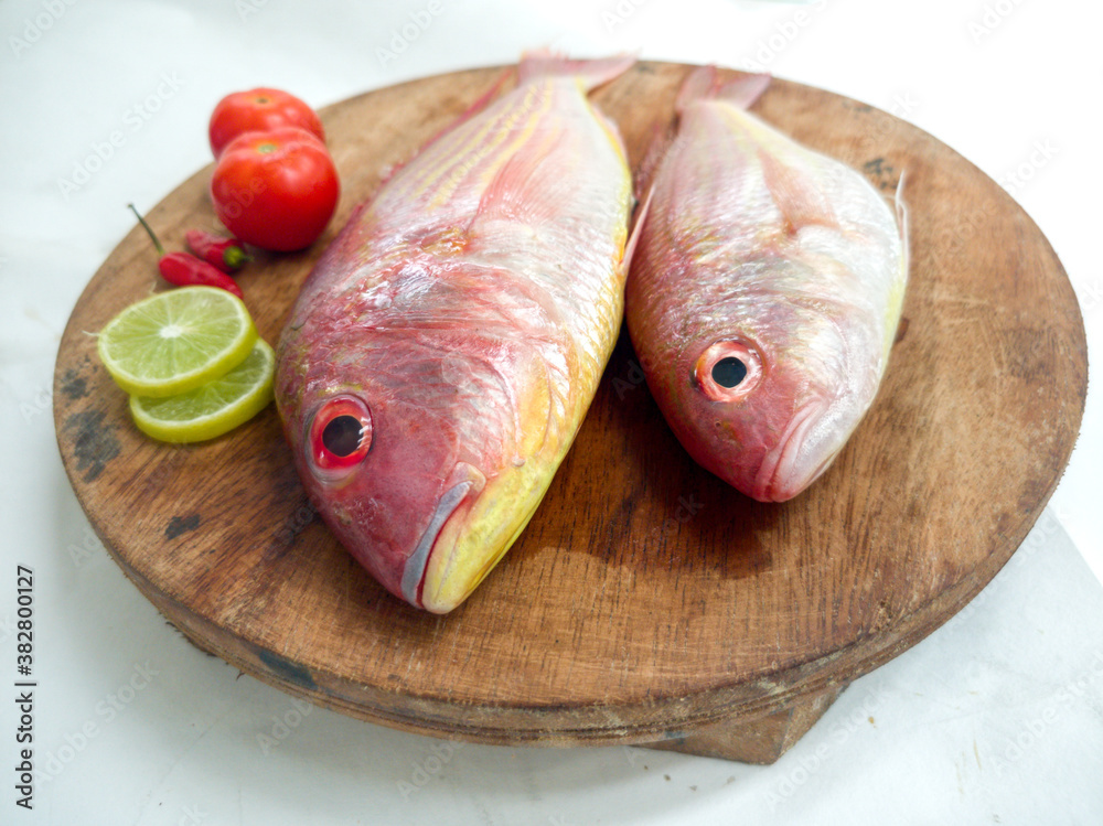 Fresh and ready to cook raw pink Perch fish with ingredients like lemon,chilli and tomatoes on a wooden pad,white background, selective focus.