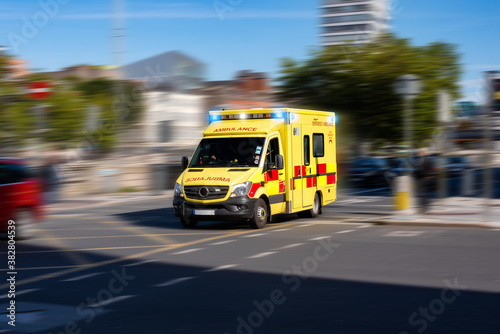 A yellow ambulance with blue lights going at high speed on the street