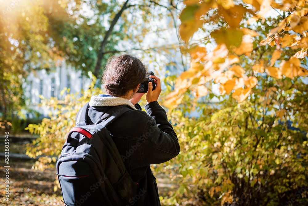 Male tourist with backpack in the park taking photos of the colorful trees on a warm sunny autumn day. Light green, yellow and orange colors of the nature around him. Male tourist with backpack in the park taking photos of the colorful trees on a warm sunny autumn day. Light green, yellow and orange colors of the nature around him.