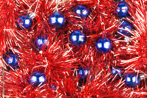 Round blue Christmas decorations lie on red tinsel as background.