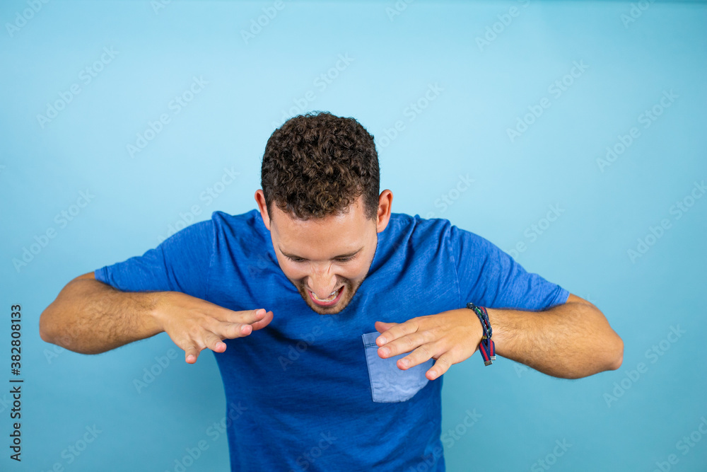 Young handsome man wearing blue casual t-shirt over isolated blue background shouting and screaming loud down with hands on mouth Young handsome man wearing blue casual t-shirt over isolated blue background shouting and screaming loud down with hands on mouth