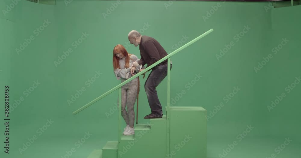 Studio, slow motion, green screen, young woman helps a senior man down the stairs, London, UK
