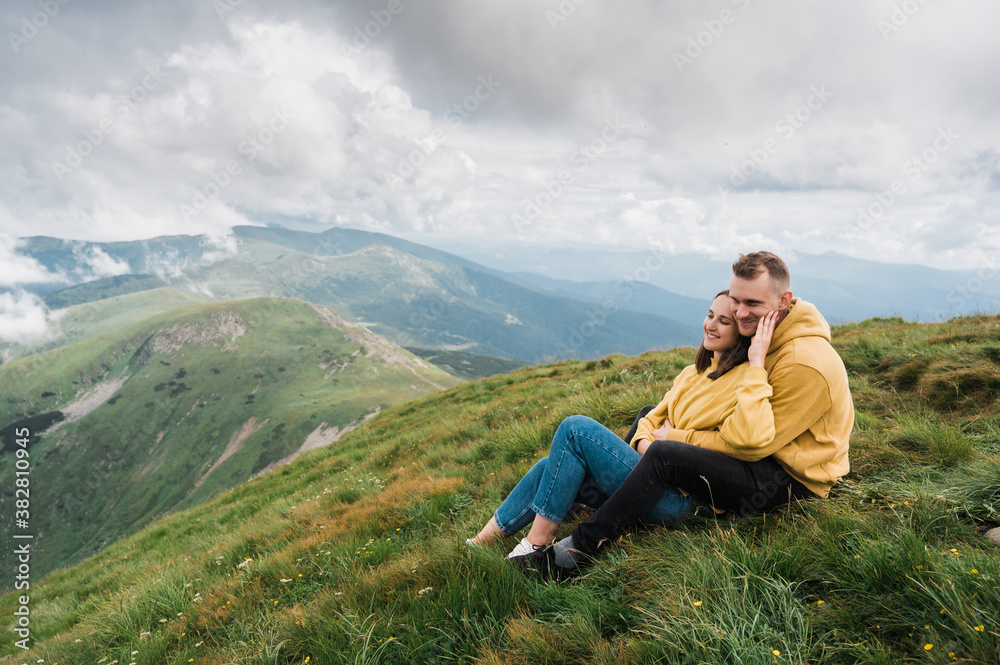 Happy couple in love sit on the top of a mountain and sensual hugging enjoying with a scenic nature views around them
