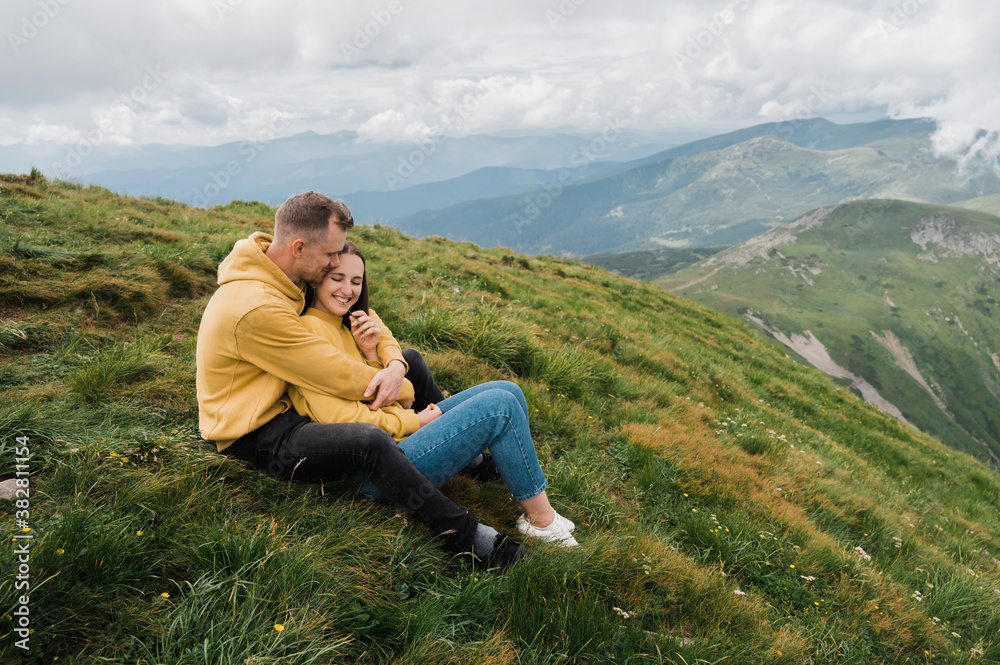 A man and a woman in love sit on the top of a mountain and sensual hugging with a scenic nature views around them