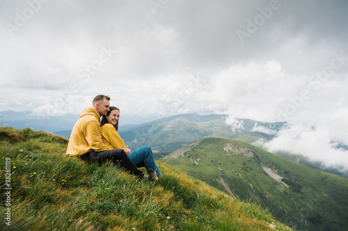 Hiking in the mountains. Couple in love climbed to the top of the mountain, they relaxing while sitting on the grass, hugging and enjoying each other and the inspiring mountain landscape