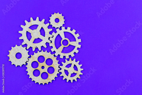 Wooden gears of different sizes on a purple background with a copy space. The concept of successful teamwork. New ideas and technologies.