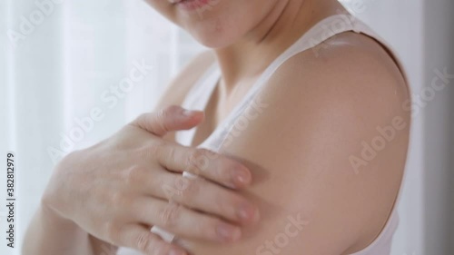 Asian woman applying lotion on shoulder and arm at home studio. white cream scrubbing to treatment skin condition.