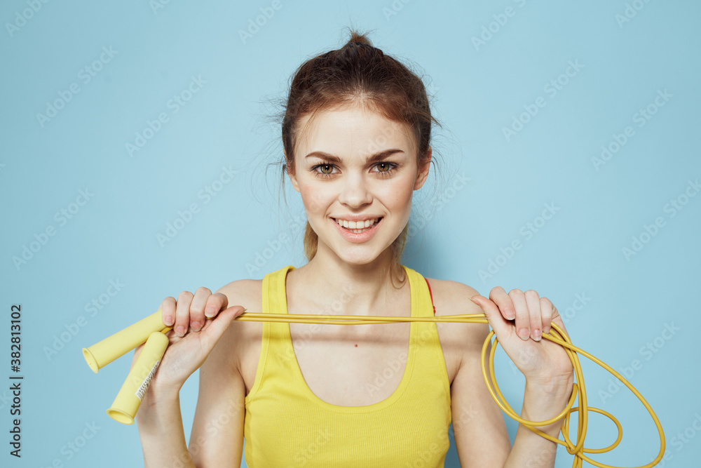 Sportive woman holding a skipping rope yellow tank top exercise gymnastics blue background Sportive woman holding a skipping rope yellow tank top exercise gymnastics blue background