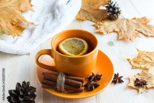 cup with hot tea and lemon, autumn leaves on the wooden background. Seasonal mood and relaxing concept