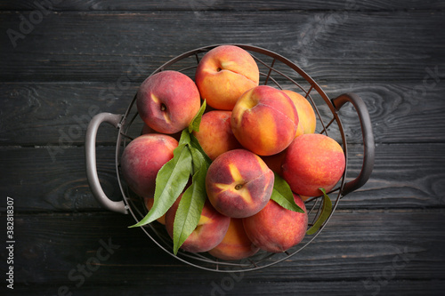 Fresh sweet peaches in metal basket on black wooden table  top view