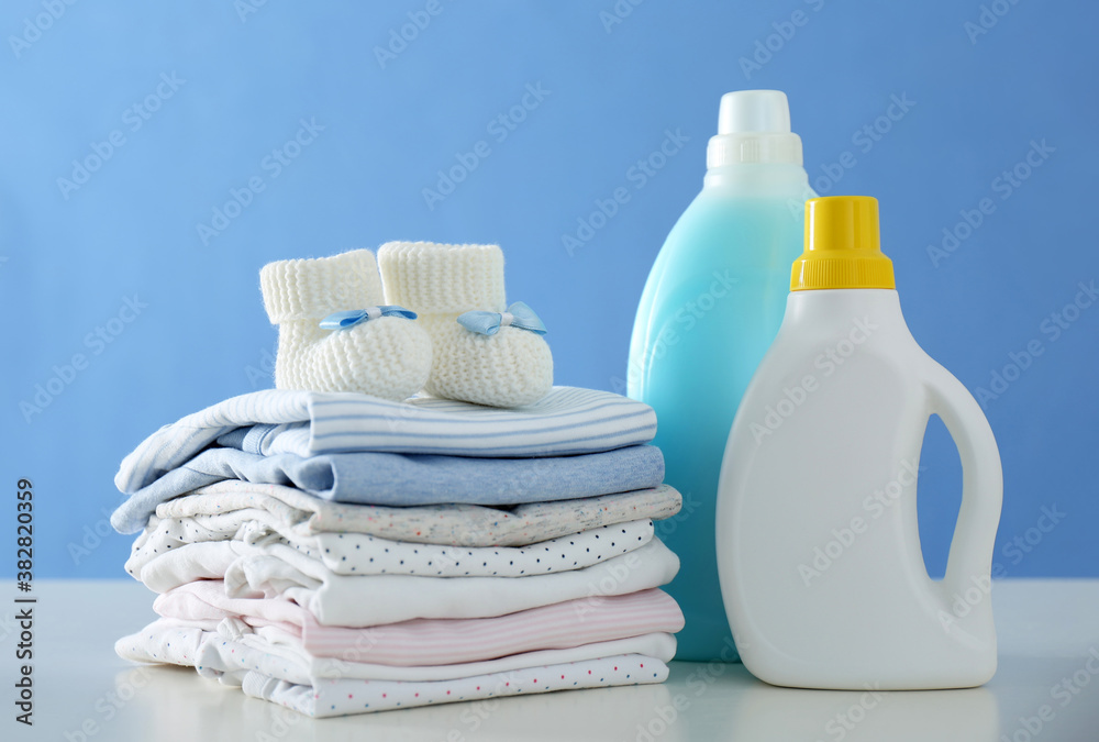 Detergents and children's clothes on white table near blue wall Detergents and children's clothes on white table near blue wall