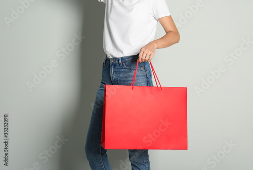 Woman with paper shopping bag on light grey background, closeup